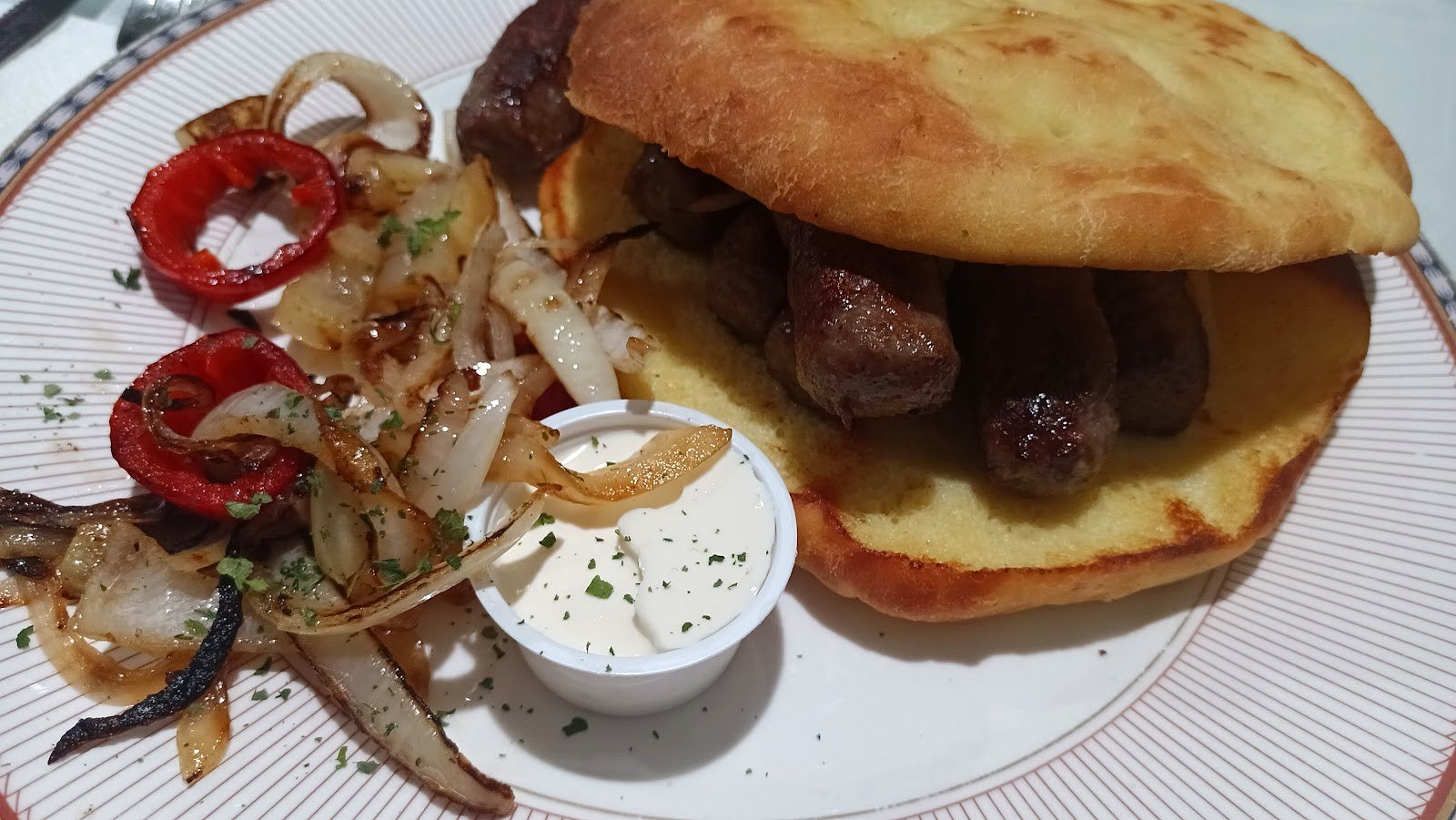 Cevapi grilled beef sausages in fresh lepina flatbread with grilled onion, roasted red pepper and kajmak
